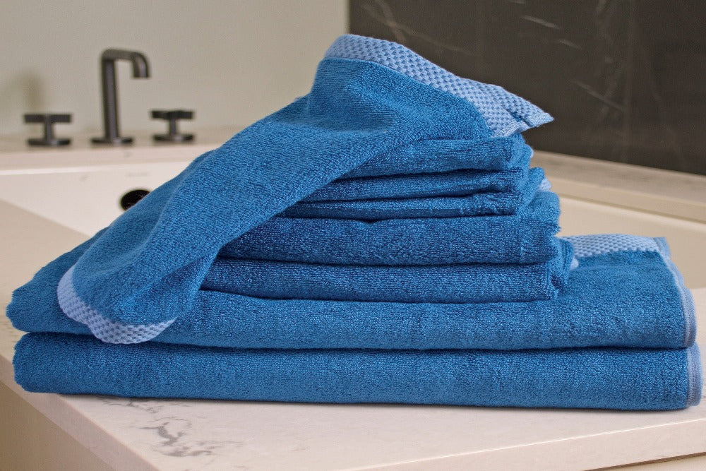 An 8 piece set of Indigo Colored Luxurious Bamboo Cotton Bath Towels stacked by size and placed on a modern well decorated vanity