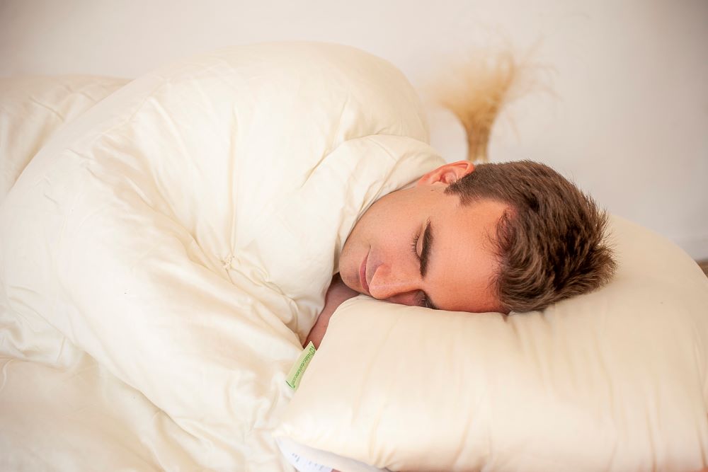 handsome man in deep sleep resting his head on a natural latex stuffed sleep pillow and snuggled into an organic cotton comforter