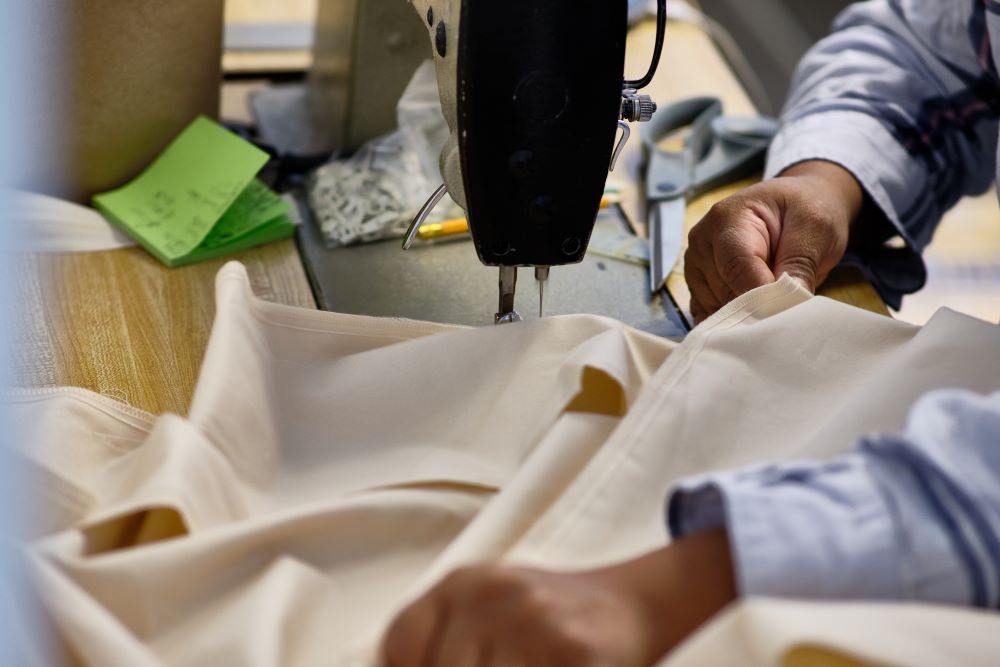 Close up view of an artisan using a specialized sewing machine to make a bed sheet from certified organic cotton material